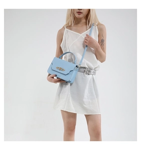 Detail of light blue leather mini bag with wavy flap and golden ring lock on white dress