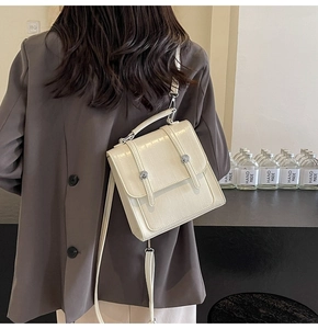 Detail of cream crocodile embossed handbag with metal buckle worn with a brown blazer