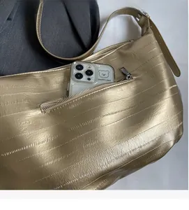 Detail of exterior zipper pocket on metallic gold textured tote bag holding a smartphone