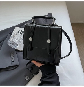 Detail of black textured leather handbag featuring silver round buckles and metallic buckles