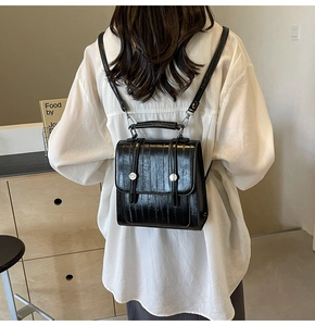 Close-up of the glossy black leather backpack featuring silver metal buttons and handle