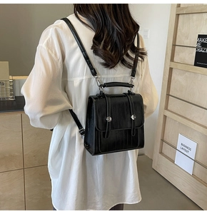 Detailed back view of a compact black textured leather backpack on a model in a minimal room