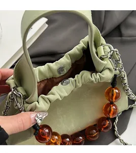Detail of light green ruched handbag featuring magnetic closure and amber bead chain