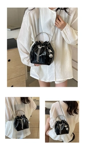 Detail of black glossy bucket bag featuring silver ring handle and chain drawstring