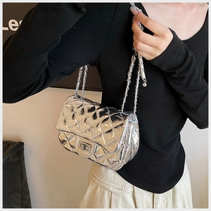 Detail of silver quilted crossbody bag with metal chain strap worn by a model