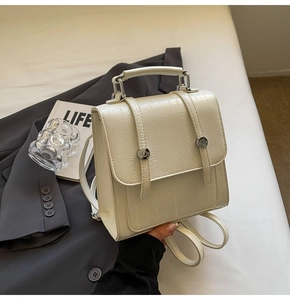 Close-up of cream textured faux leather mini backpack with metal buckle and top handle