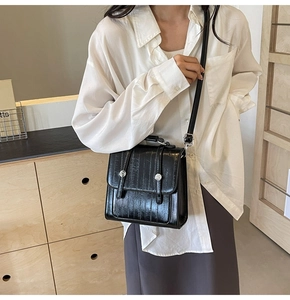 Close-up of black glossy crocodile textured leather handbag with silver metal buckles