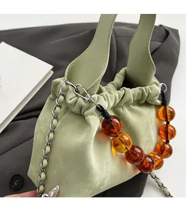 Detail of light green PU handbag featuring amber beaded chain and silver metal strap