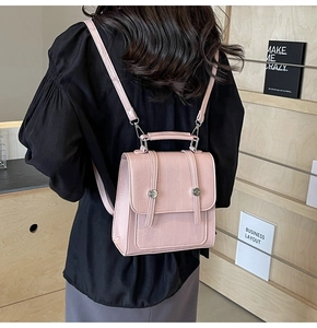 Detail view of pink croc-embossed mini backpack on model in a stylish interior setting