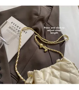 Détail d'un sac seau matelassé beige avec chaîne dorée sur fond de blazer marron