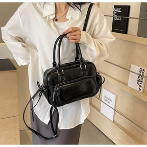 Detail of black PU leather handbag showing a front zipper pocket and side bow tie accent