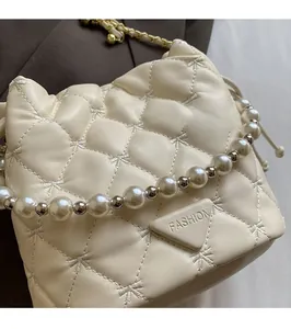 Détail d'un sac seau matelassé blanc avec chaîne en perles et logo métallique élégant