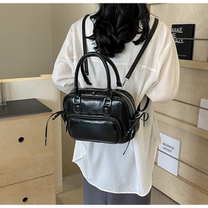 Model wearing a black faux leather backpack with bow details and front zipper pocket