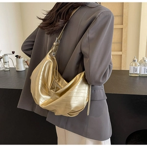 Macro view of metallic gold textured crossbody bag with soft pleats on stylish wide strap