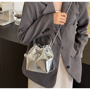 Detail of silver metallic bucket bag with textured handle and chain strap on a cafe table