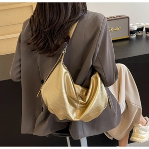 Detail of gold pleated texture on metallic underarm bag worn with a casual grey blazer