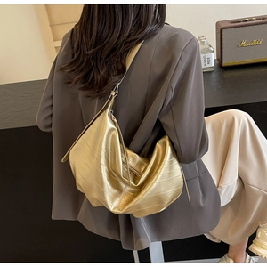 Macro shot of a large golden metallic hobo bag with horizontal pleats on a gray suit