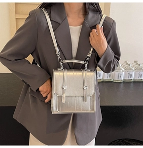 Detail of silver metallic rectangle backpack with textured finish and silver hardware buckles