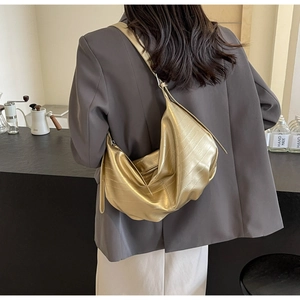 Chic gold crescent crossbody bag with crocodile pattern worn over a dark grey blazer