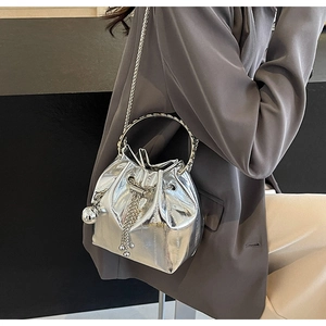 Detail of silver metallic bucket bag with drawstring and chain strap on grey blazer