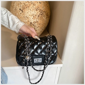 Detail of glossy black quilted bag with silver twist lock and chain strap