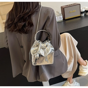Detail of silver metallic bucket bag with metal ring handle and chain strap on model