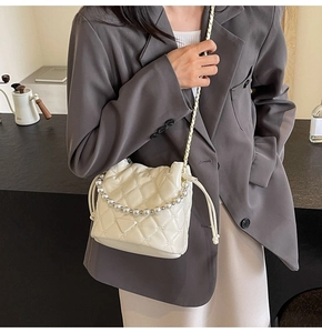 Détail du sac seau blanc matelassé avec anse en perles et bandoulière chaîne dorée