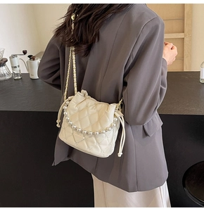 Détail d'un sac seau matelassé beige avec poignée en perles et bandoulière sur modèle
