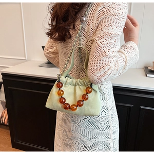 Detail of light green ruched bucket bag with large amber beaded handle on white lace dress