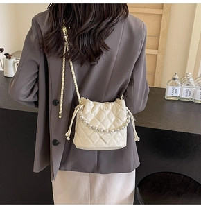Vue arrière d'un mannequin portant un sac seau matelassé crème avec anse en perles