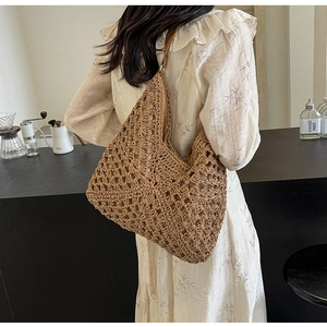 Detailed view of hollow knit straw tote bag with brown leather strap on model