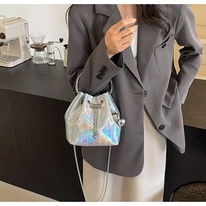 Chic silver laser bucket bag with metal ring handle and chain strap shown in a cafe