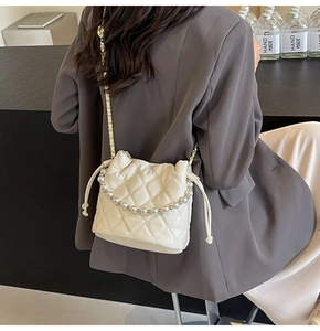 Détail du sac seau matelassé crème avec lanière en perles et chaîne dorée à l'épaule