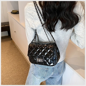 Detail of black quilted crossbody bag with silver clasp and leather woven chain strap