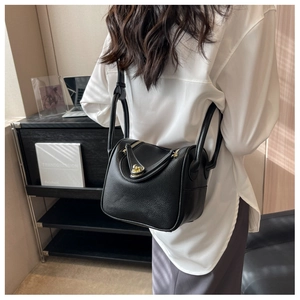 Sac Lindy en cuir grainé noir avec détails dorés porté à l'épaule par un mannequin