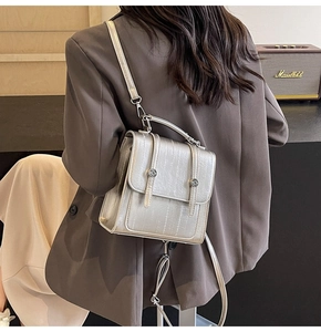 Detail of silver textured backpack with metal buckles shown on a model in urban setting