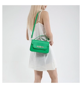 Green leather handbag with golden rectangular lock shown on model wearing white dress