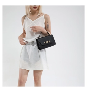 Detail of elegant black matte leather handbag with golden hardware clasp on white dress