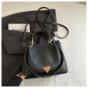 Close-up of black leather tote bag with gold triangle plaque and slim shoulder strap
