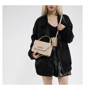 Detail of beige crossbody bag with gold metal buckle and leather texture on a model