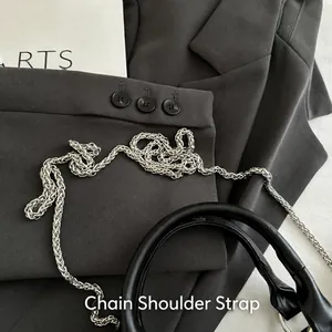 Details von silberner Kettenriemen und zylindrischem Ledergriff an schwarzer Modetasche