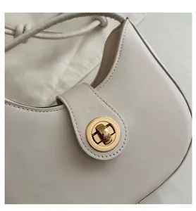 Close-up of a white crescent shoulder bag featuring a golden circular twist lock and strap