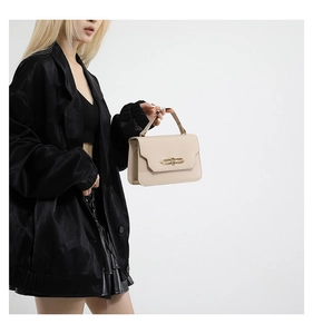 Detailed shot of beige stylish handbag with gold metal clasp on a black blazer outfit