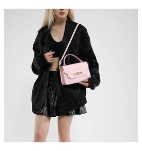 Close-up of light pink crossbody bag with gold buckle on a model in studio setting