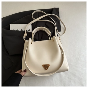 Close-up of cream white PU leather tote bag with gold triangle logo on a white cloth