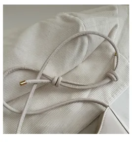 Detail of cream white leather shoulder strap with decorative knot and gold metal tips