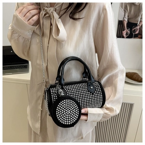 Detalle de bolso cilíndrico negro con tachuelas plateadas, cadena y monedero a juego