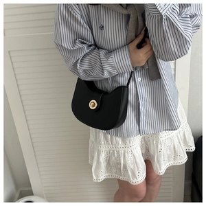 Close-up of black half-moon shoulder bag with elegant gold circular rotary lock
