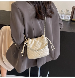 Détail du sac seau matelassé crème avec bandoulière en perles et plaque en métal triangulaire
