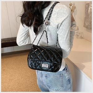 Detail shot of a black quilted crossbody bag with silver chain strap worn by a model